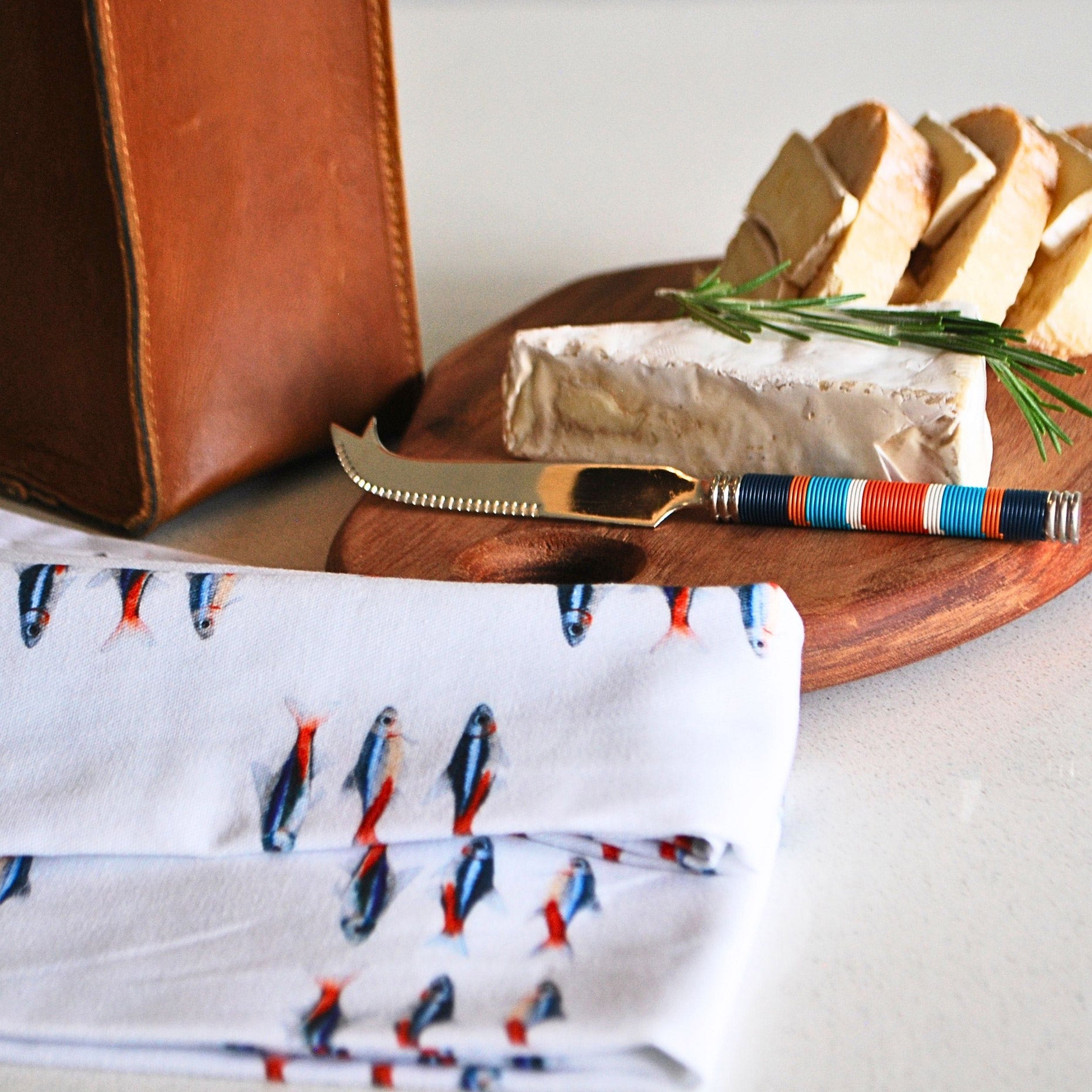 Umekela Essentials Box (Pieter de Jager Oblong Cheese Board, Pieter de Jager Leather Single Wine Carrier, PaulaG Cheese Knife Sea Boat Blue, Owl in the Moss Neon Napkins Close Up)